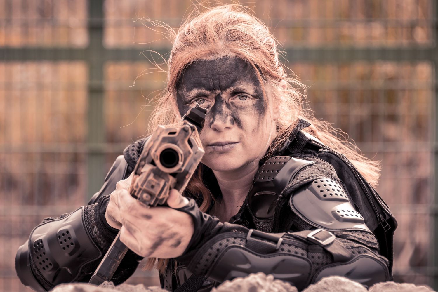 Woman in tactical gear with face paint aiming a pistol during a military-style training exercise.