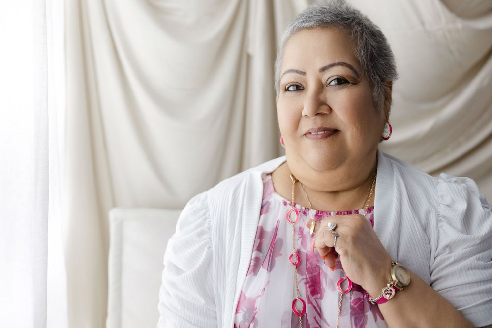 Smiling middle-aged woman with short gray hair wearing a floral top and white cardigan, posing confidently indoors.