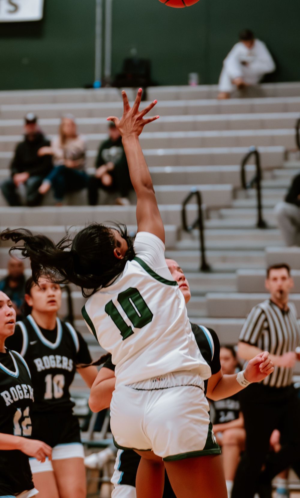 Basketball player in white jersey leaps high to grab rebound during intense game action.
