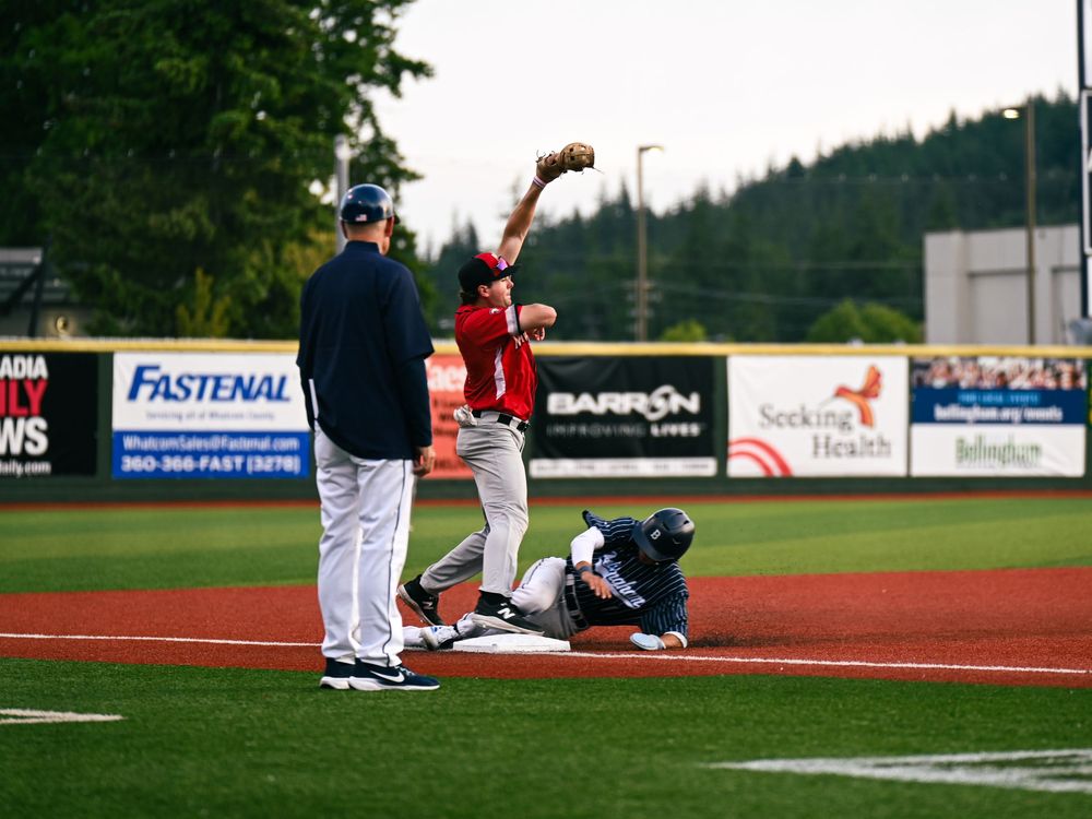 Baseball players positioned on a field during a game with advertising banners visible in the background.