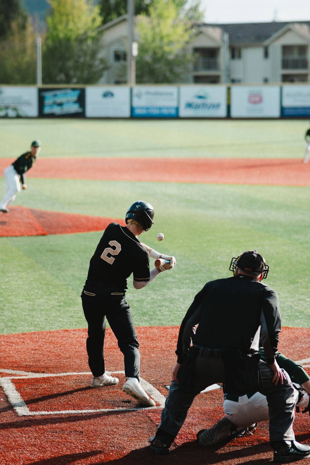 Baseball player at bat with catcher and umpire during game on red dirt field.