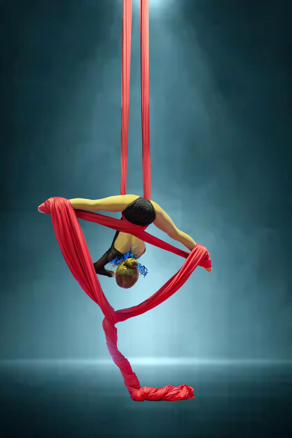 Focal Point Images
Aerial artist performs inverted pose using red silks in atmospheric blue-lit studio.