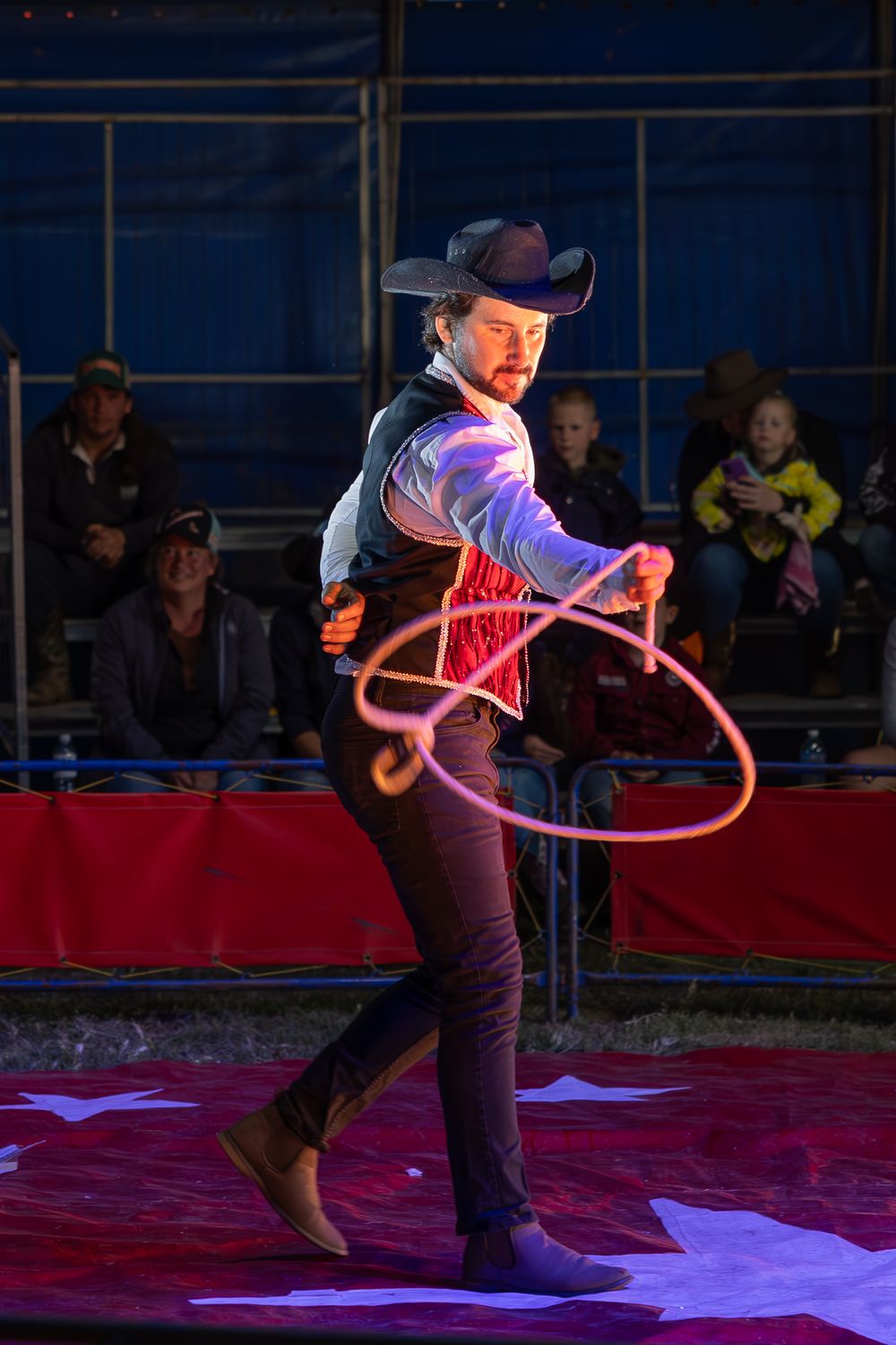 Performer spins illuminated lasso rope during western-themed circus act.