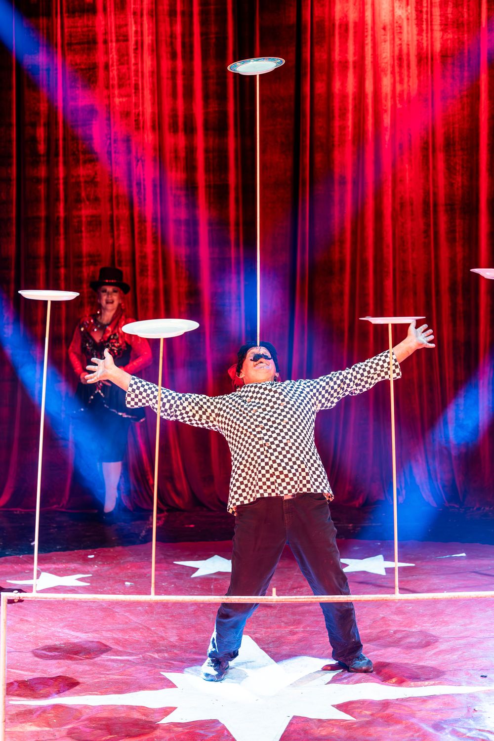 Focal Point Images
Plate spinner performs balancing act on illuminated stage with red curtain backdrop.