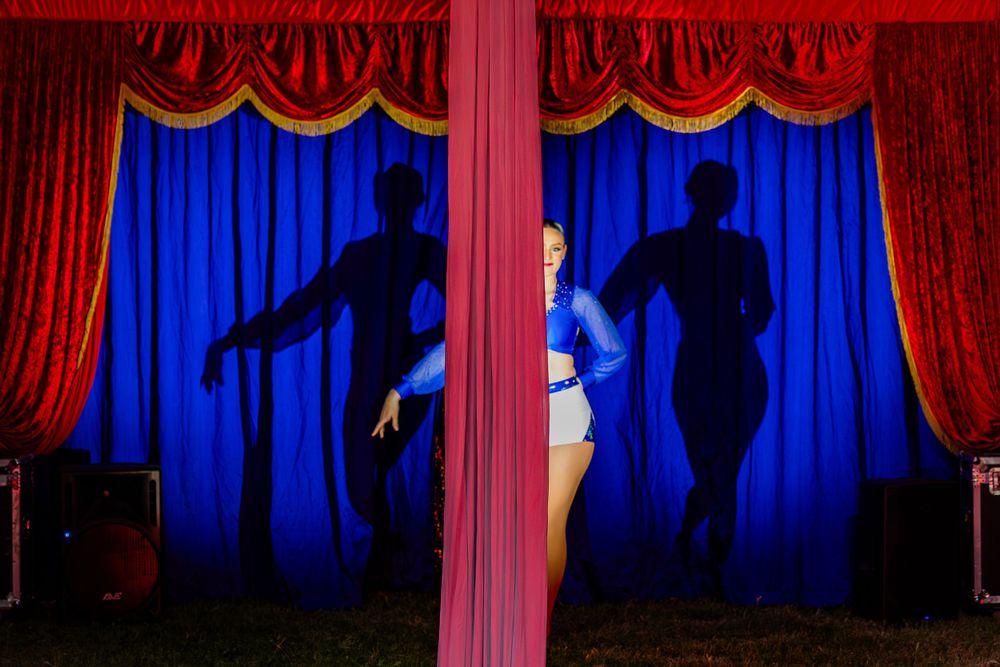 Performer silhouetted against blue curtain casting dramatic shadows on stage.