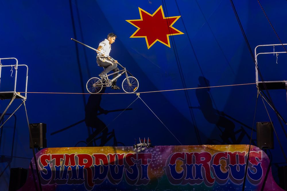 Silhouetted cyclist performs dangerous balancing act on high wire under red star decoration.