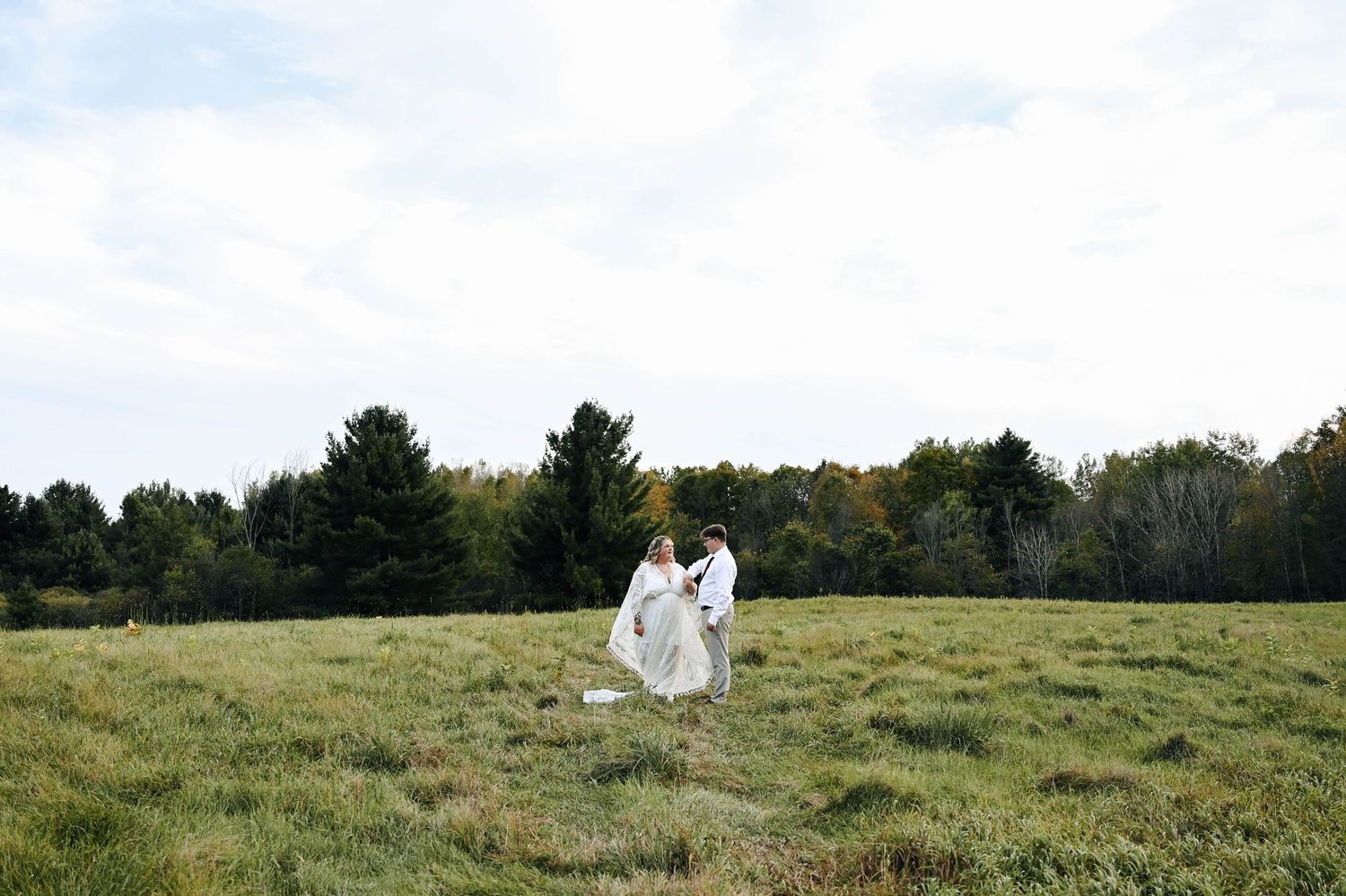 Two figures in white walk across vast green field under cloudy sky.