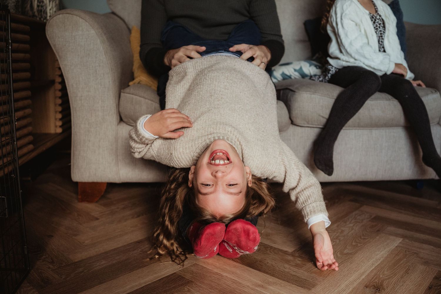 A person lying on a wooden floor in a cozy living room setting with white furniture in the background.
