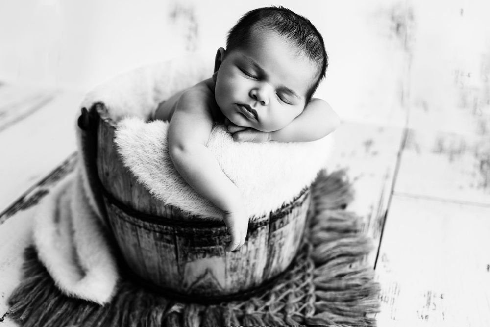 A sleeping newborn baby swaddled in white blankets lies peacefully in close-up black and white photography.