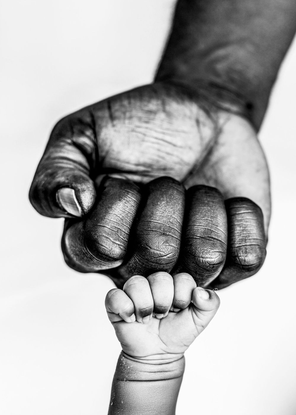 A black adult hand gently holds a baby's tiny fist in a powerful black and white photograph symbolizing unity and protection.Nova DMV DC