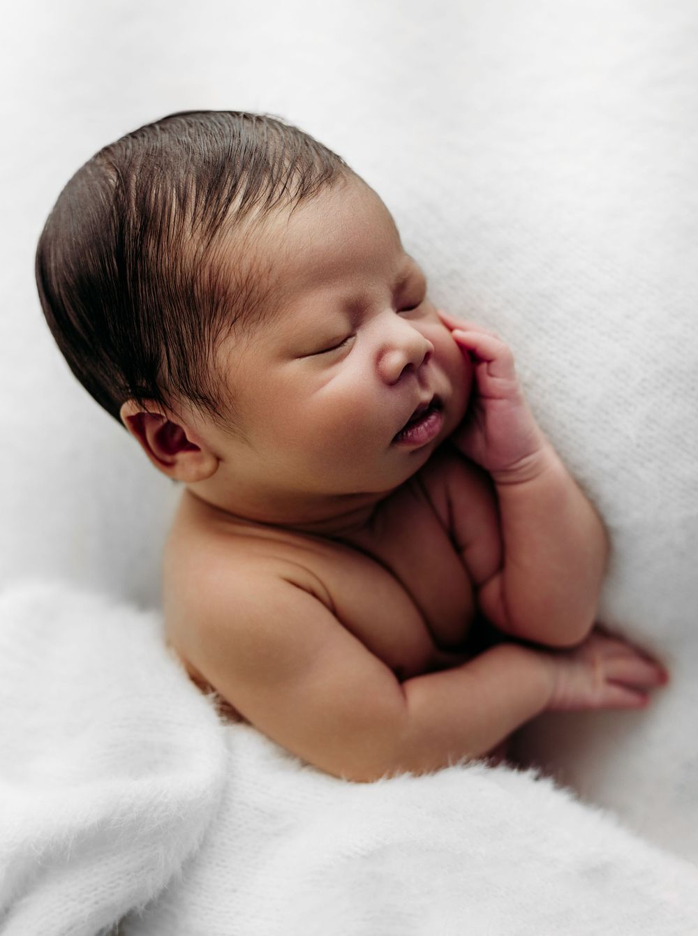Peaceful newborn baby sleeping on soft white blanket with hand resting near face in gentle natural light.
in Fairfax, VA Nova photo DMV