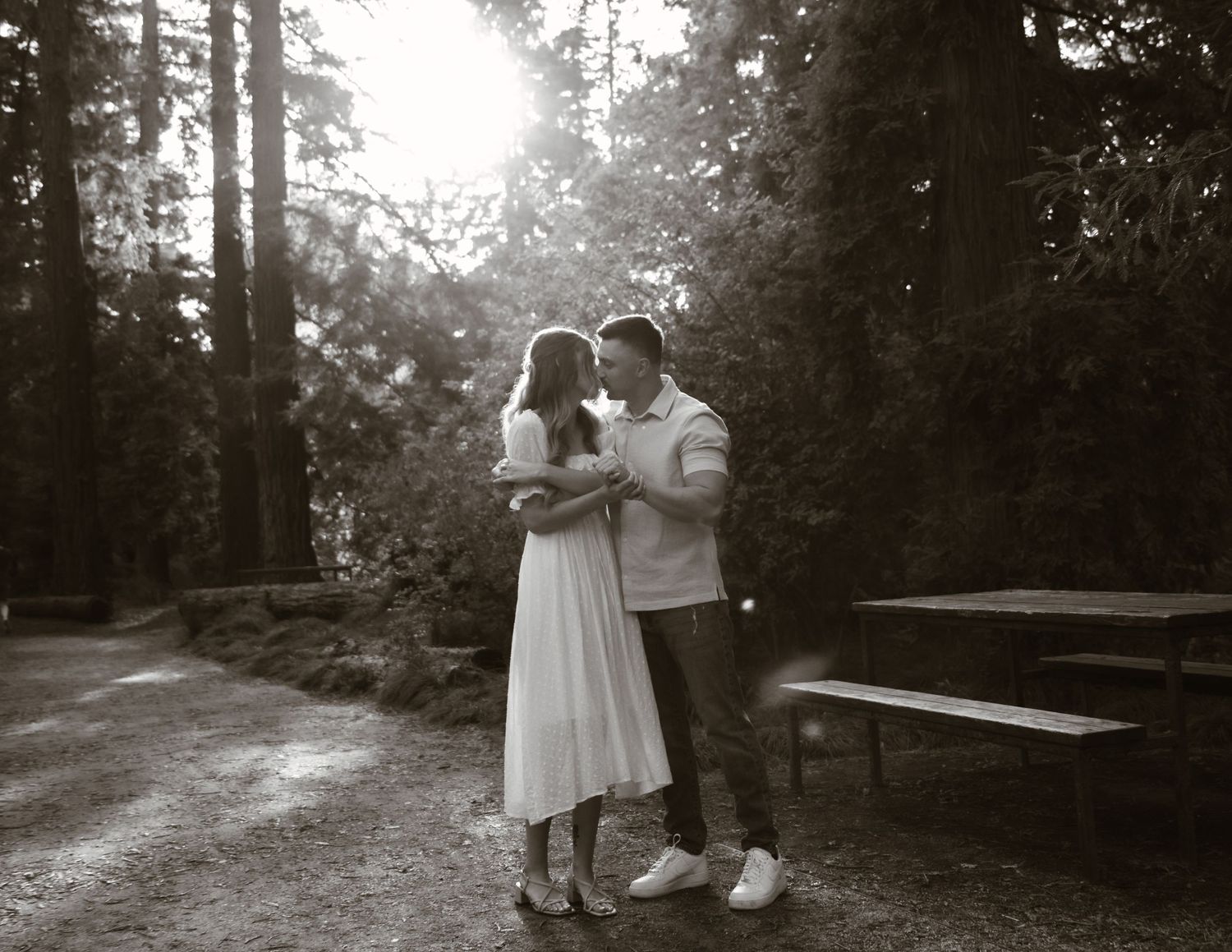 A couple embraces in a dreamy black and white forest setting.