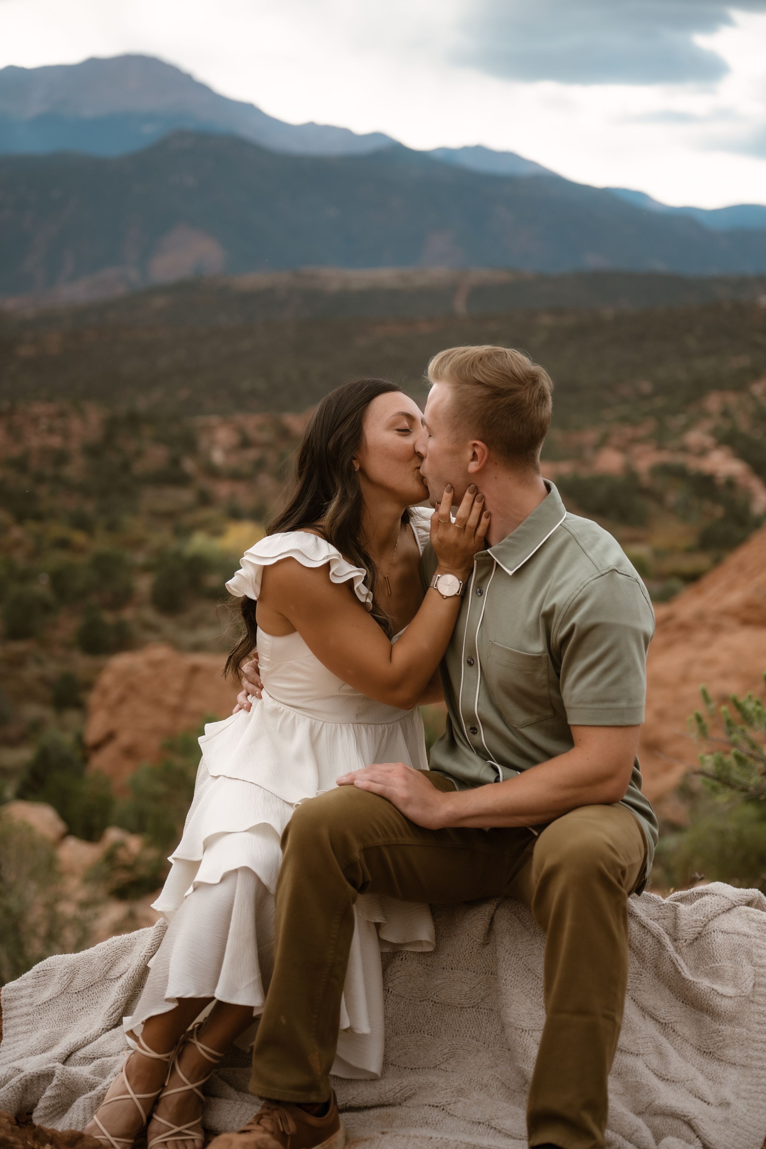 A tender embrace shared between a couple sitting on rocky terrain with mountain views.