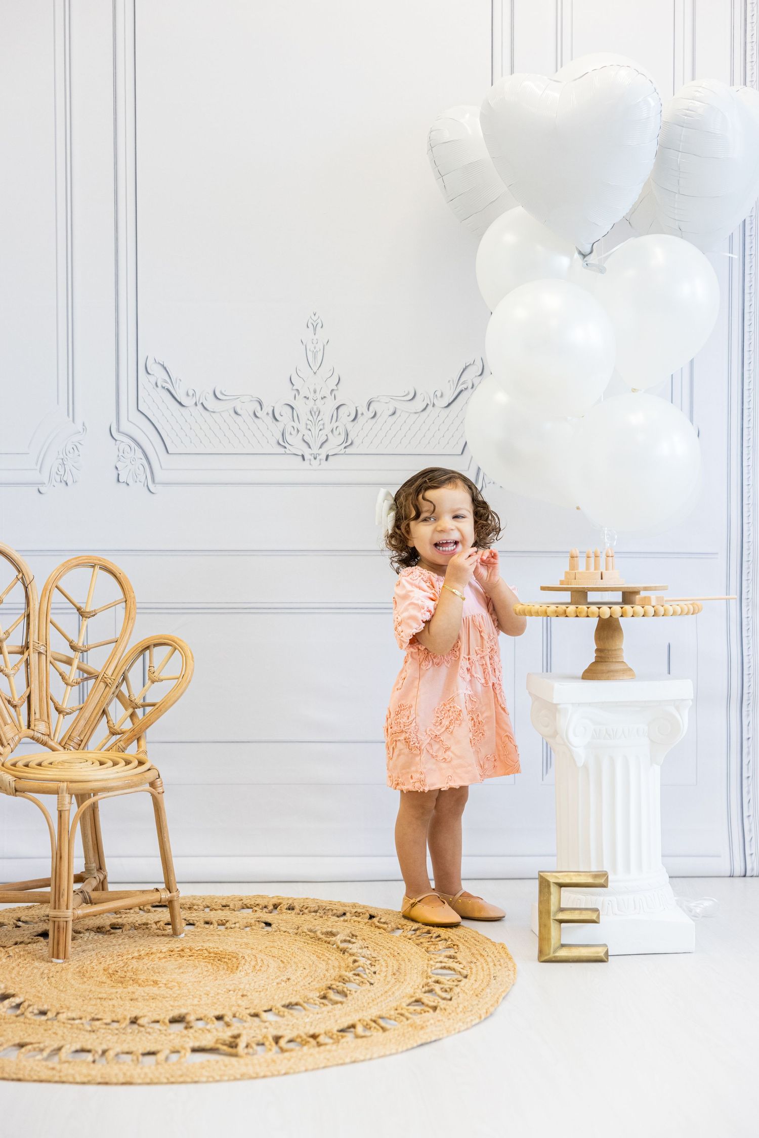 Child poses with white heart balloons in elegant room with gold accents.