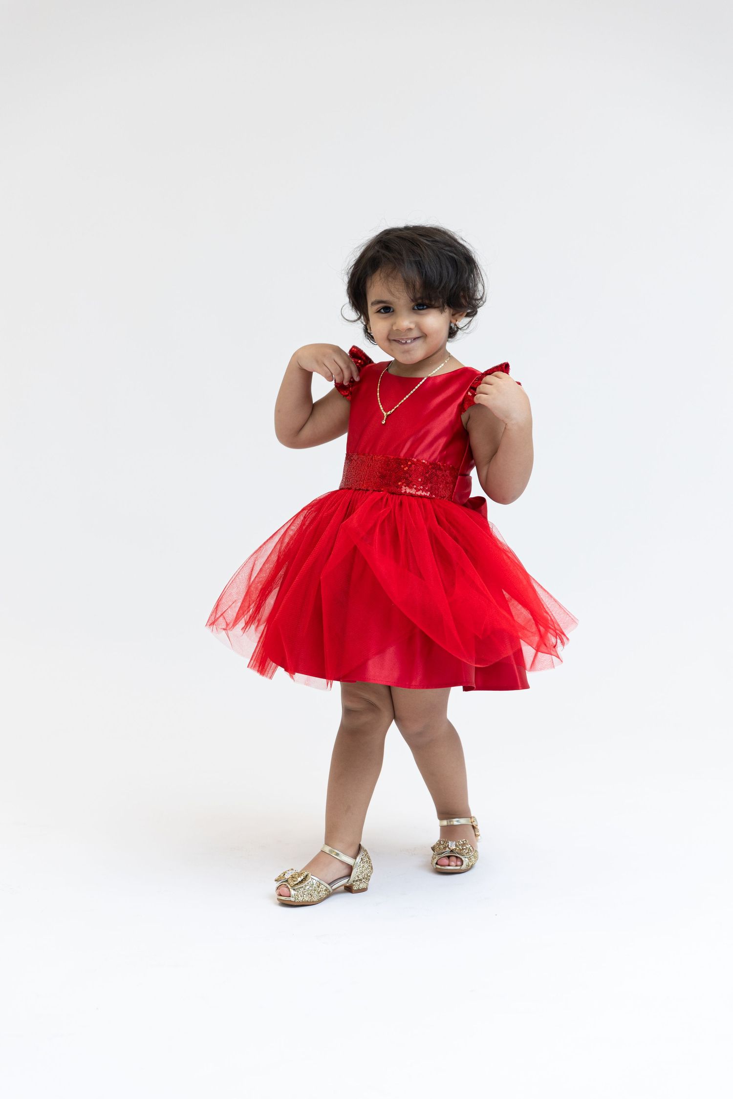 Young dancer twirling in bright red tulle dress against white background.