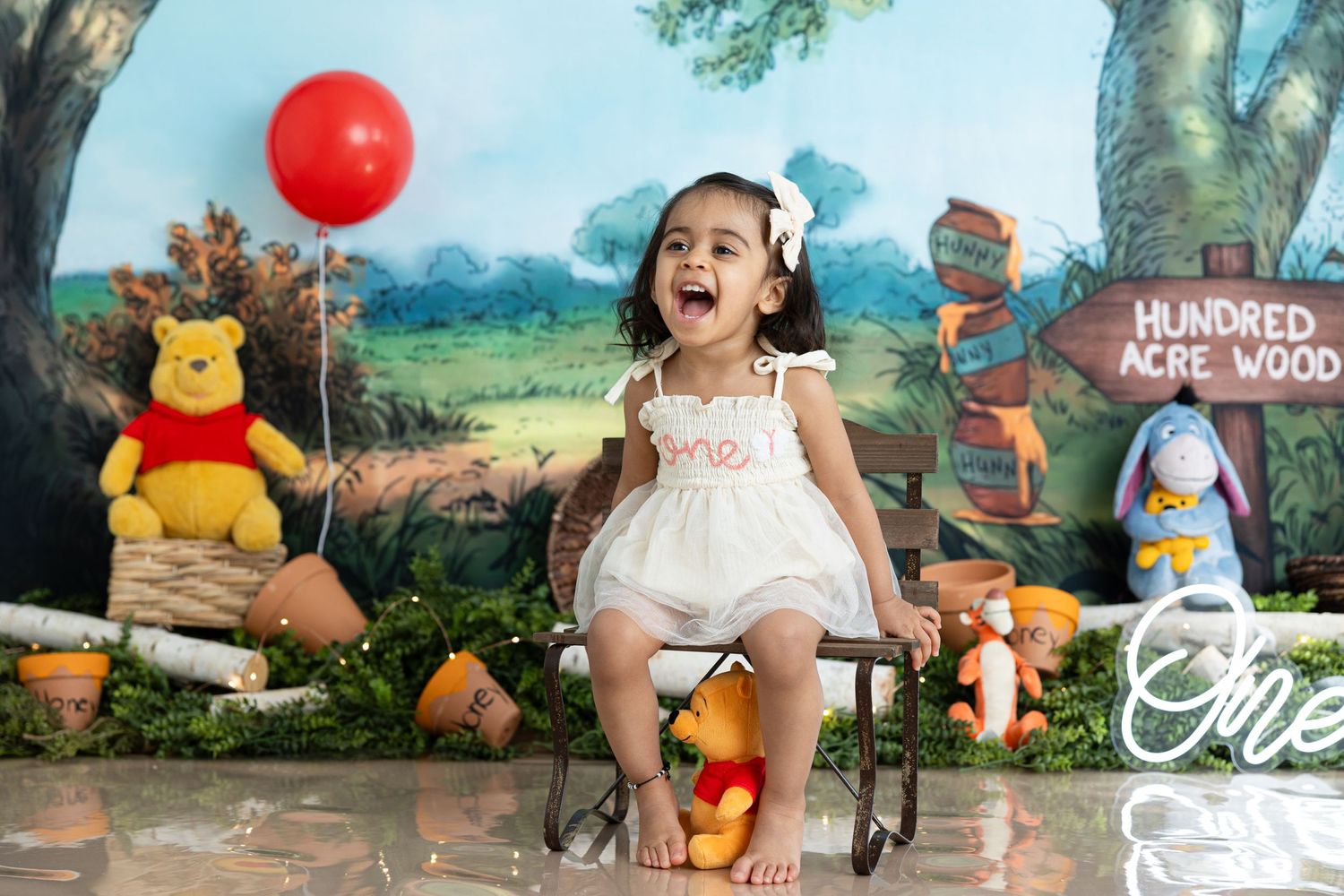 Whimsical photo of child with Winnie the Pooh themed backdrop and red balloon.