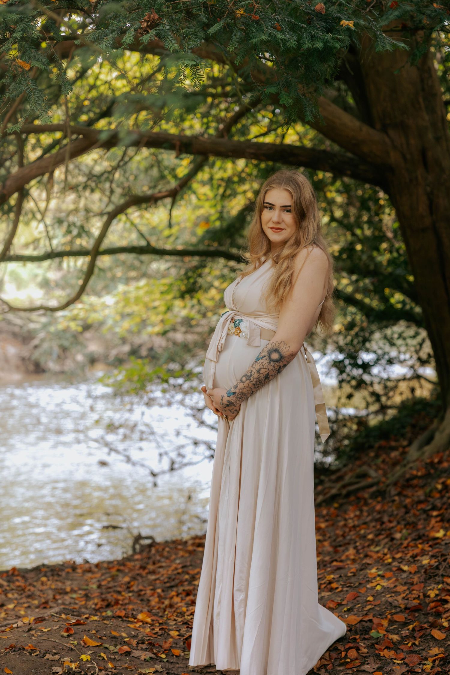 Autumn maternity portrait by a river with fall foliage in the background.