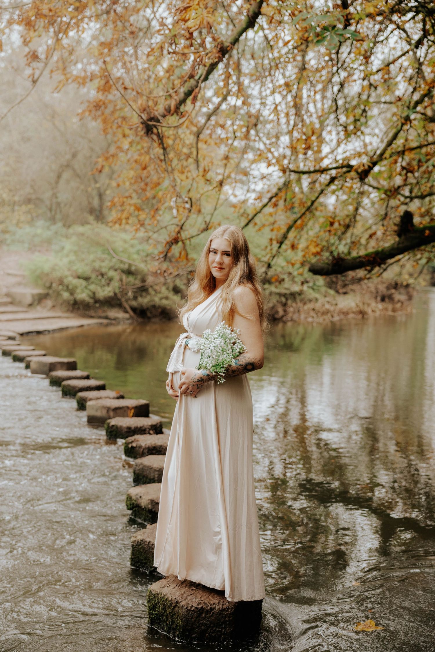 Ethereal maternity photo on stepping stones over a river during autumn.