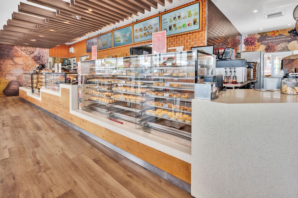 Panoramic view of a bright bakery interior with wood accents, display cases, and counter service area.