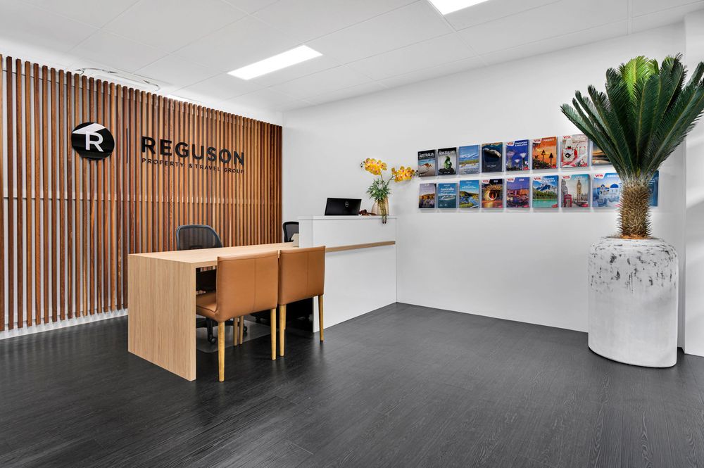 Modern office reception area with wooden slat wall, white desk, and colorful artwork displays on the wall.