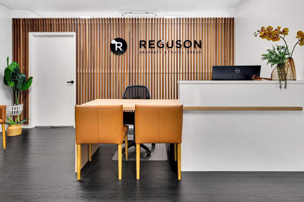 Modern office reception area with wooden slat wall, white counter, orange desk, and decorative plants.