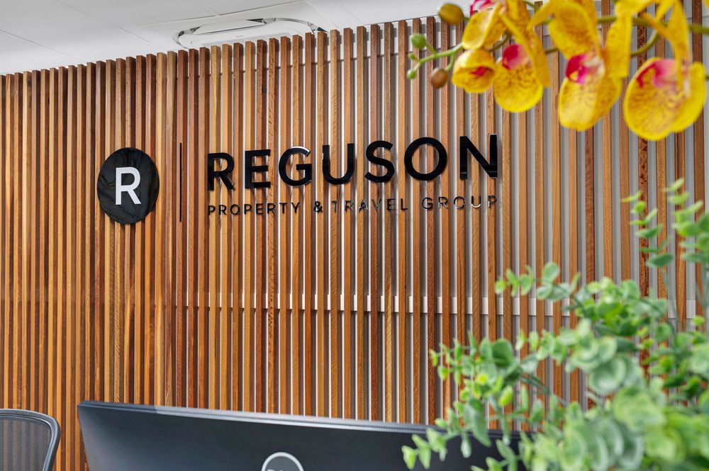 Modern outdoor dining area with wood slat wall, yellow orchids, and Reguson signage in an elegant setting.