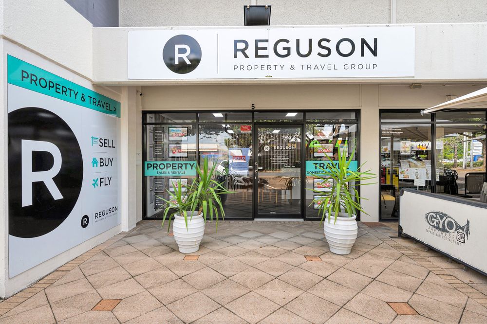 A panoramic view of a modern office entrance with white walls, glass doors and the Reguson company logo.