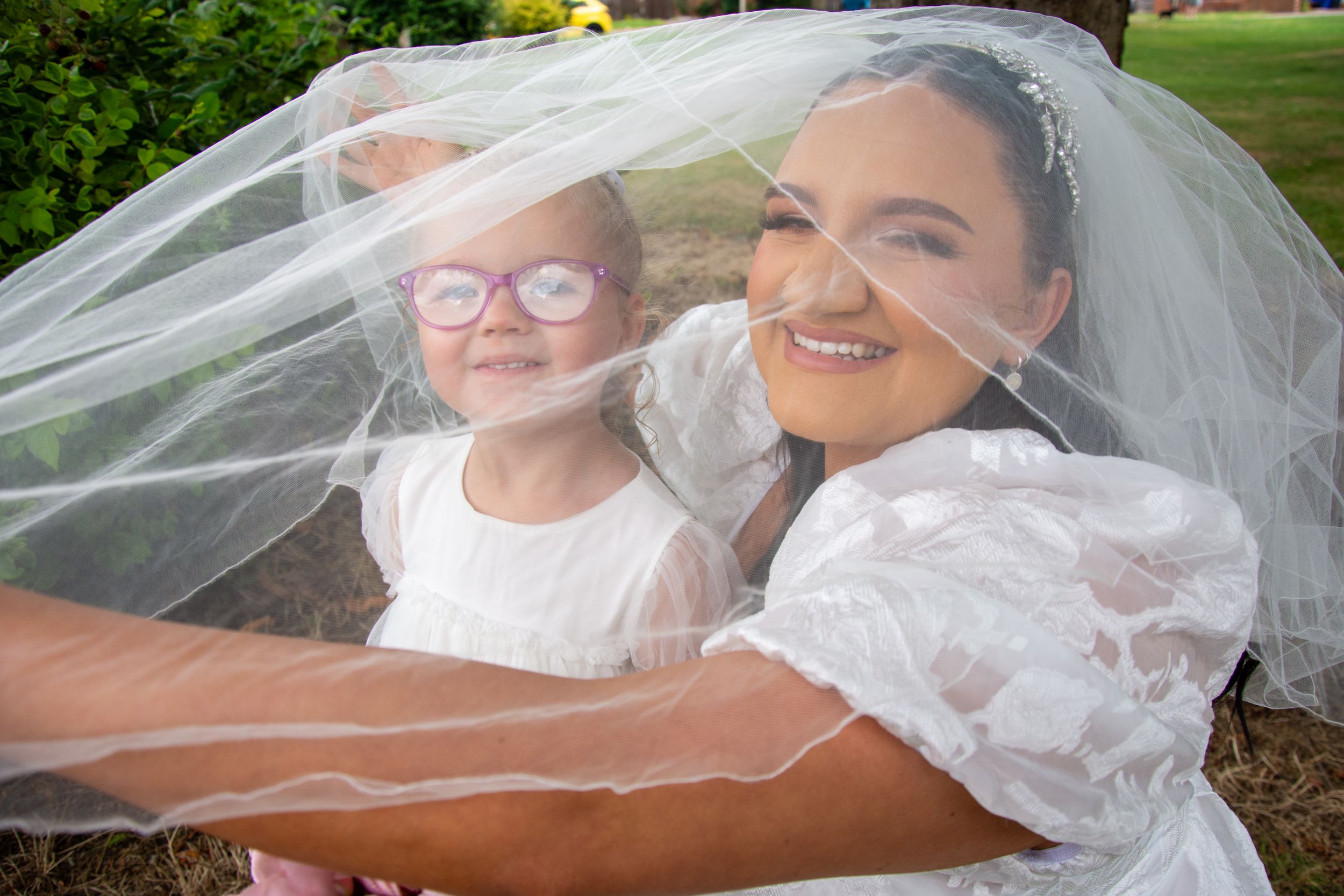 A joyful moment shared under a flowing white wedding veil outdoors.