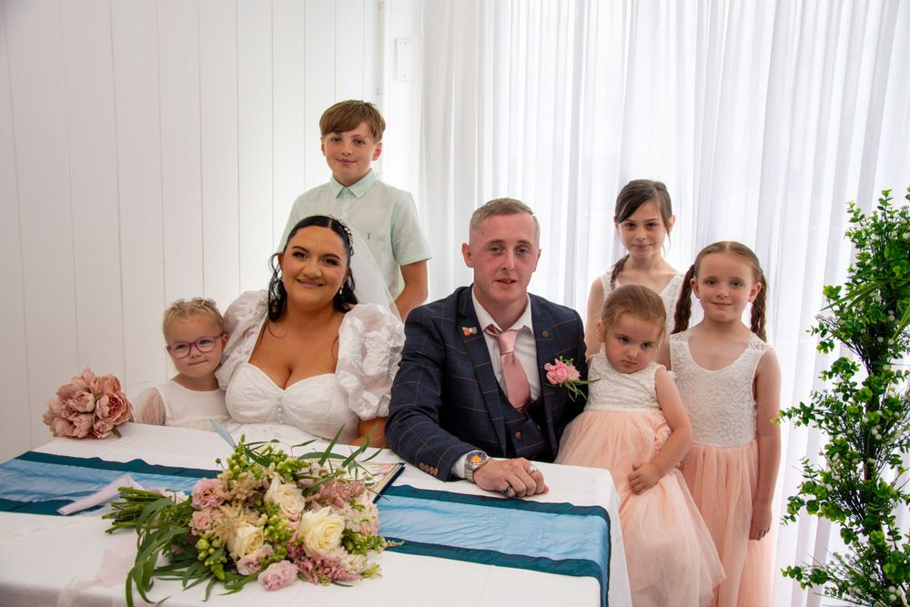 Wedding party gathers around signing table with floral decorations.