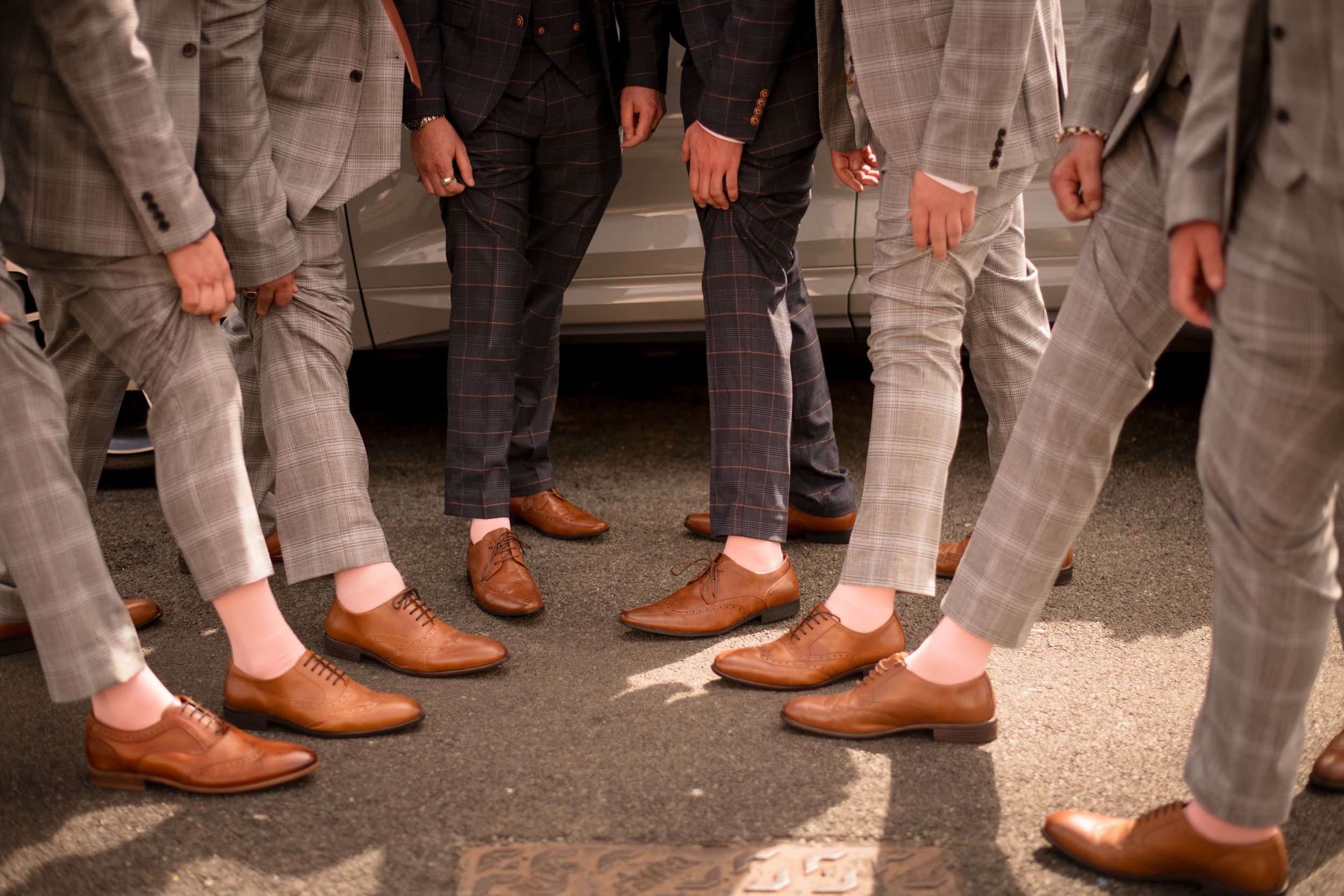 Groomsmen show off their coordinated brown leather dress shoes and gray pants at a wedding.