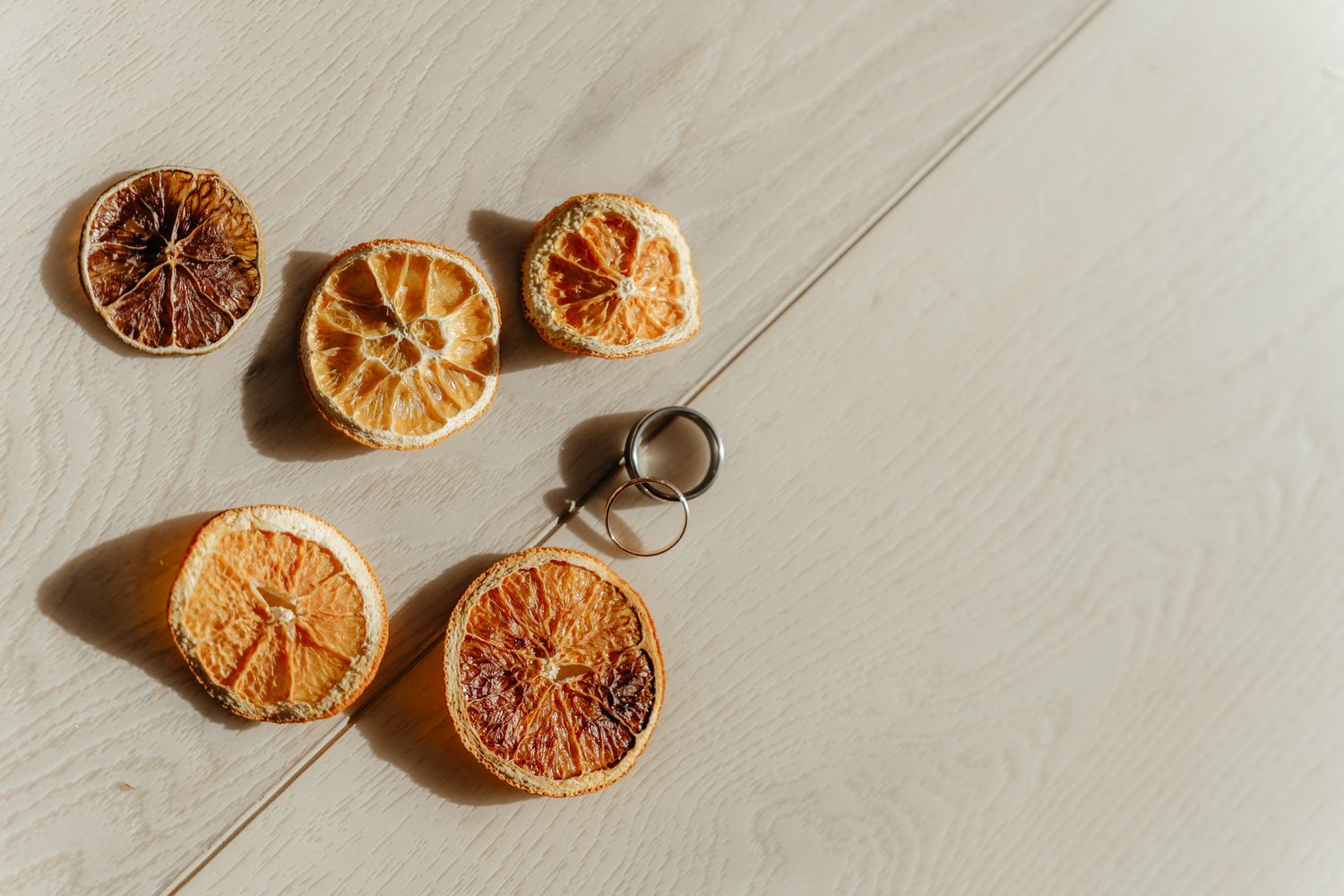 Dried orange slices scattered on a light wooden surface with dramatic shadows and a small metal ring.