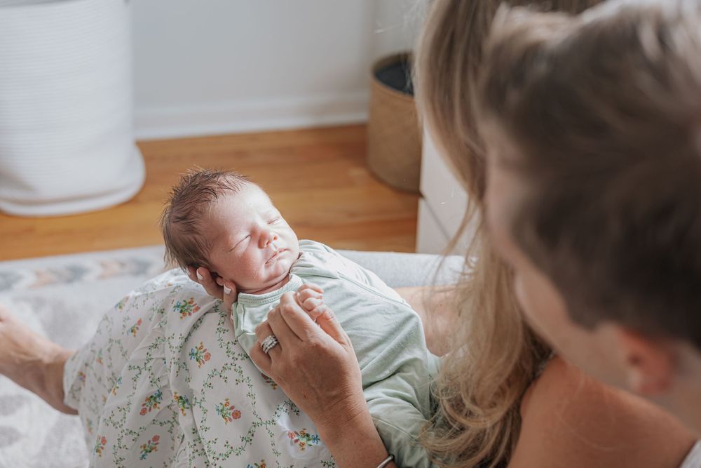 Parents lovingly gazing at their swaddled newborn baby wrapped in a floral blanket during an indoor newborn photo session.