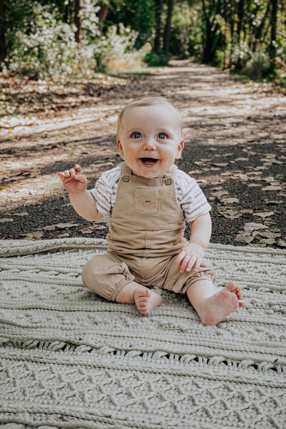 A smiling baby wearing tan overalls and a striped shirt sits on a knitted blanket outdoors in a series of photos.