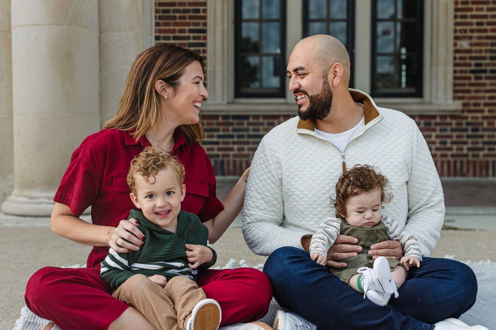 Family sitting on ground outside brick building sharing genuine laughter together.