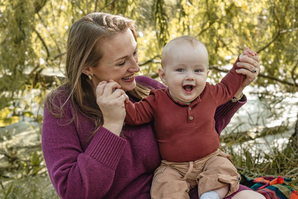 Parent and baby sharing joyful moments together outdoors in autumn lighting.