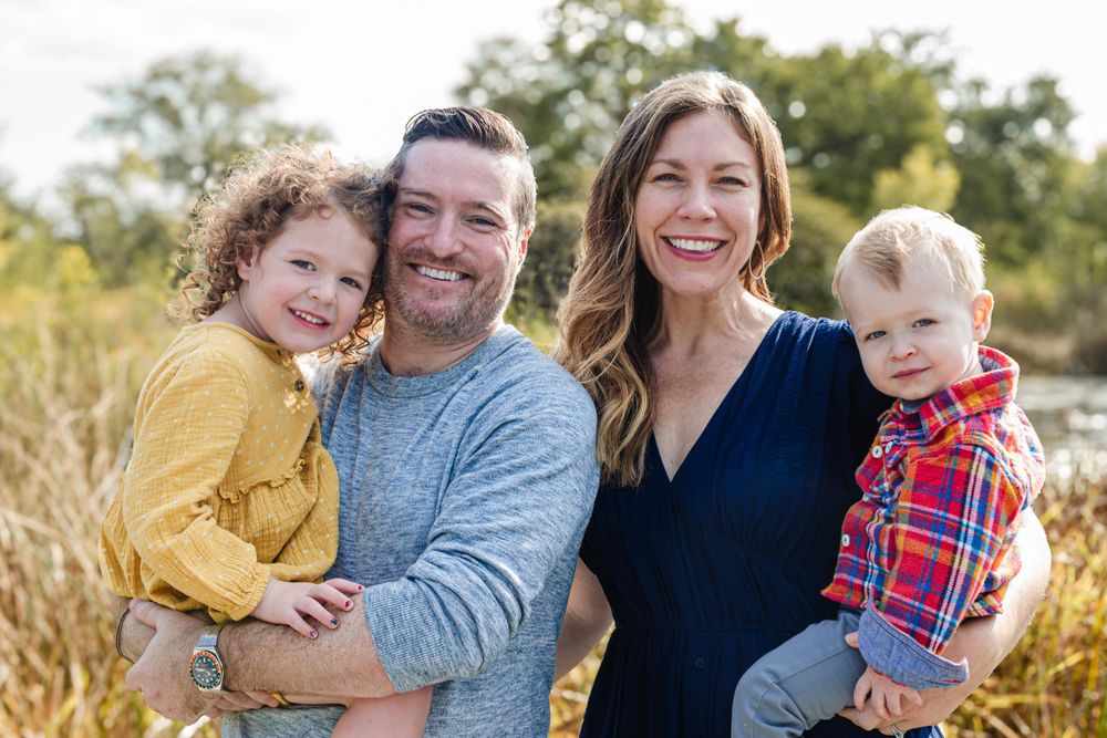 A cheerful family of four posing together in a sunny field with golden grass.