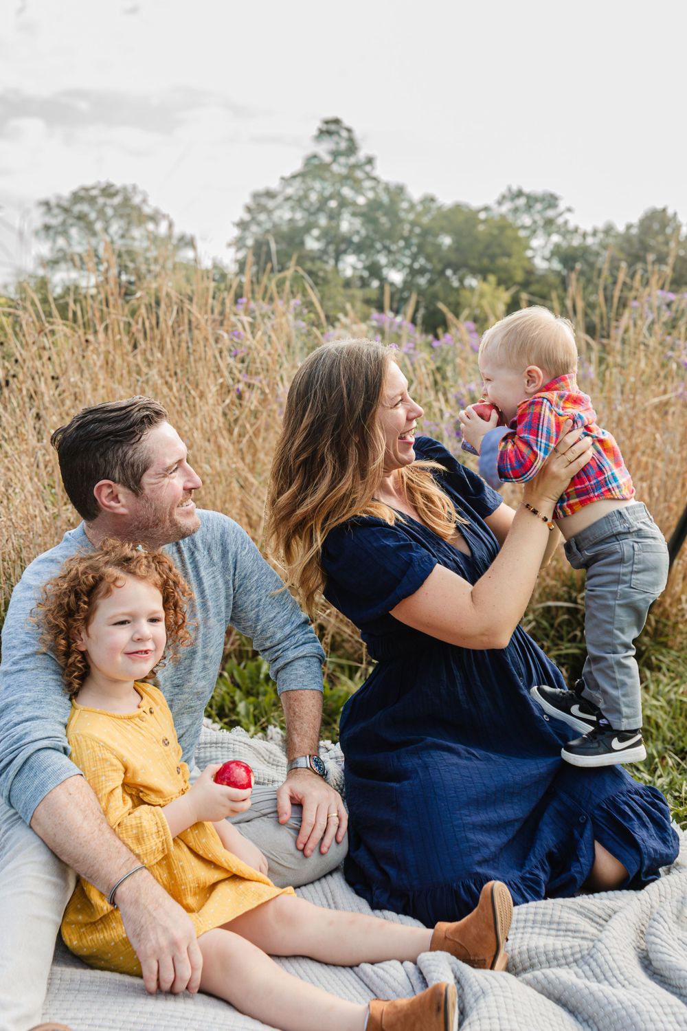 Family enjoying a picnic outdoors with children in yellow dress and plaid shirt.