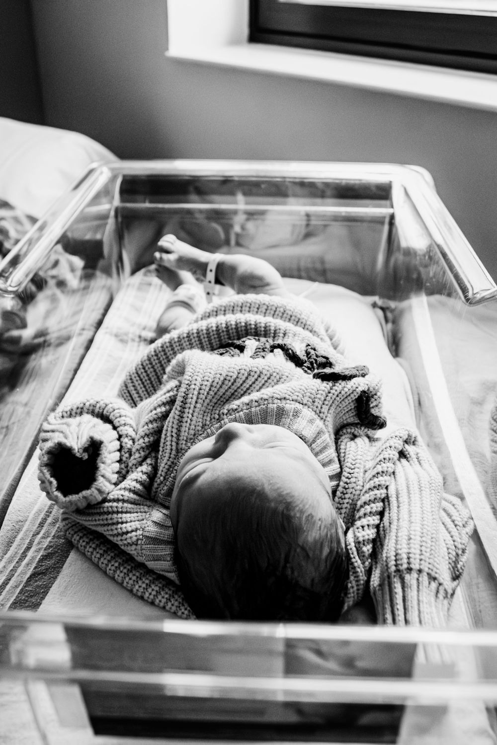 Sequence of black and white photos showing a sleeping newborn baby in a hospital bassinet wearing a striped blanket.