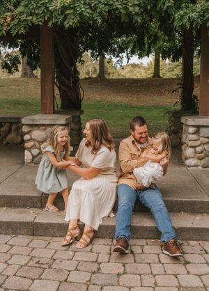 A family sits together on stone steps under trees in a casual outdoor setting.