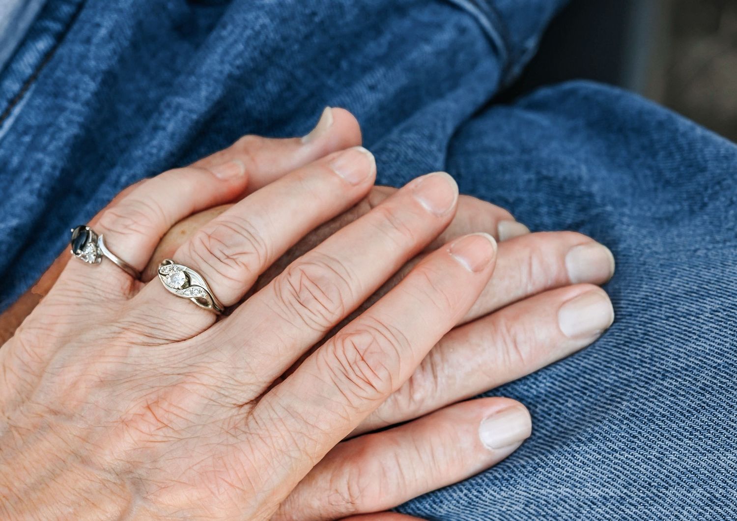 a older couple celebrating their 50th anniversary.  a close up of them holding hands with their rings showing.
