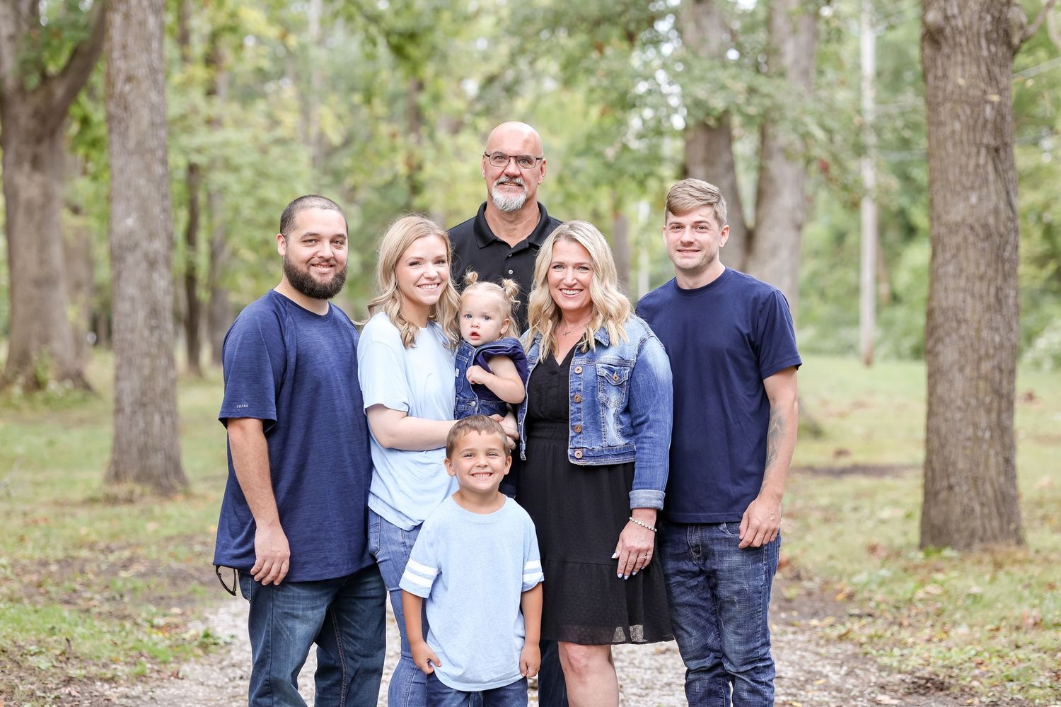 A loving family poses together for a group photo outdoors among tall pine trees on a sunny day.