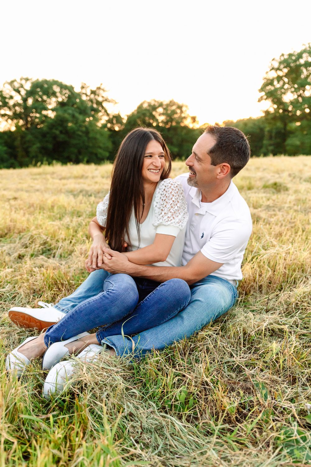 Couple lounging in grassy field during golden hour engagement session.