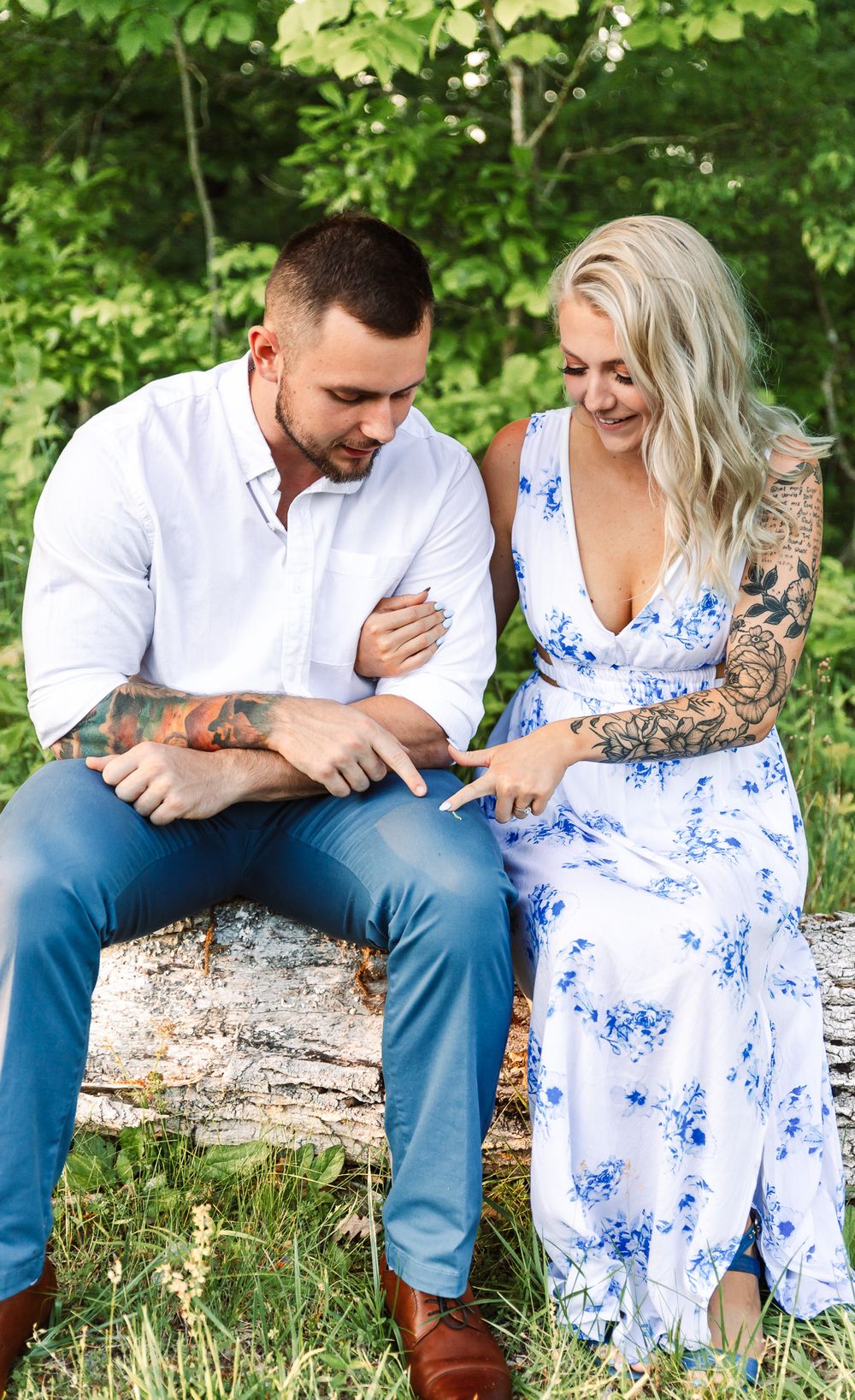 Couple shares tender moments while sitting on fallen log in green forest setting.