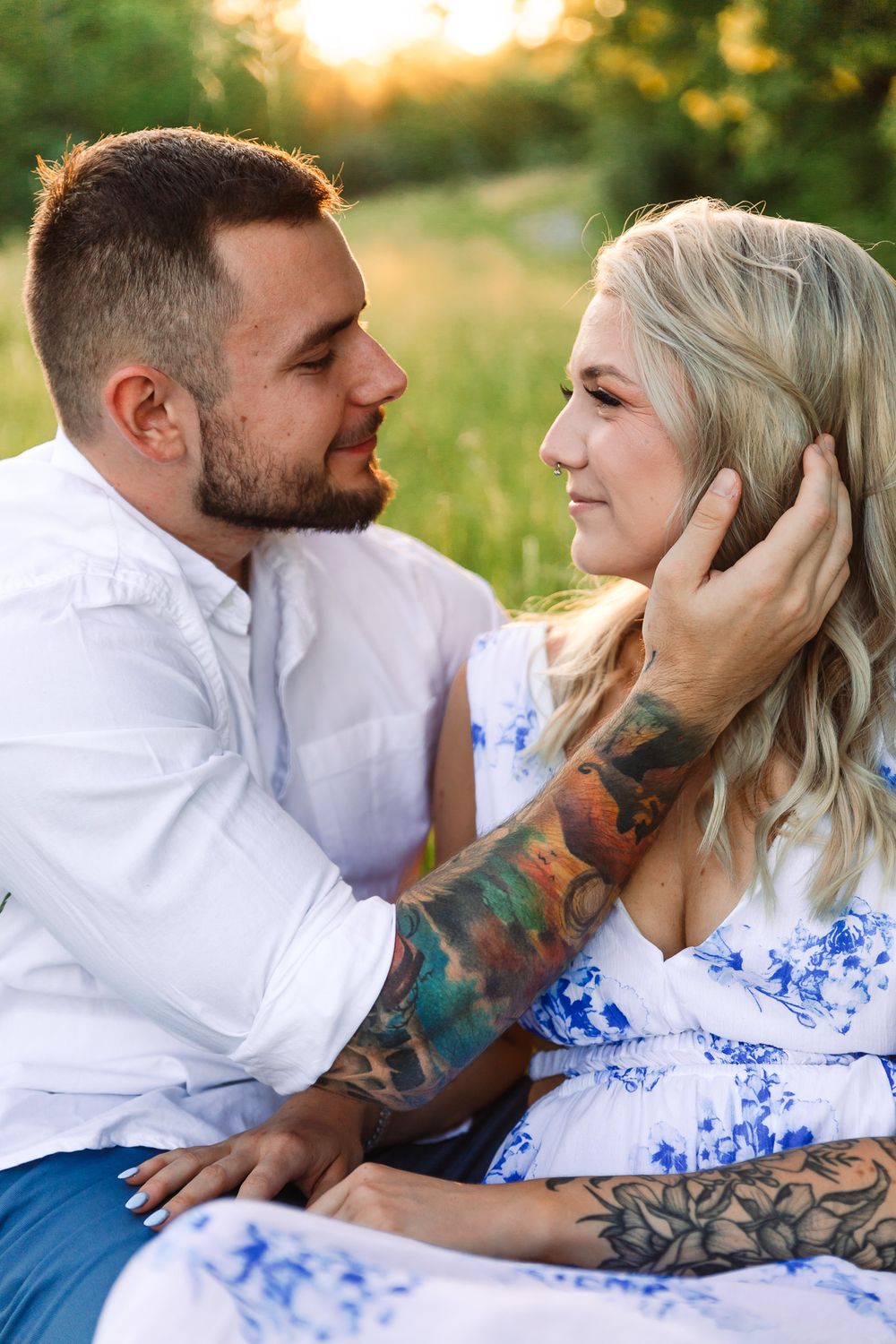 Romantic couple in white and blue outfits embracing in a sunlit meadow.