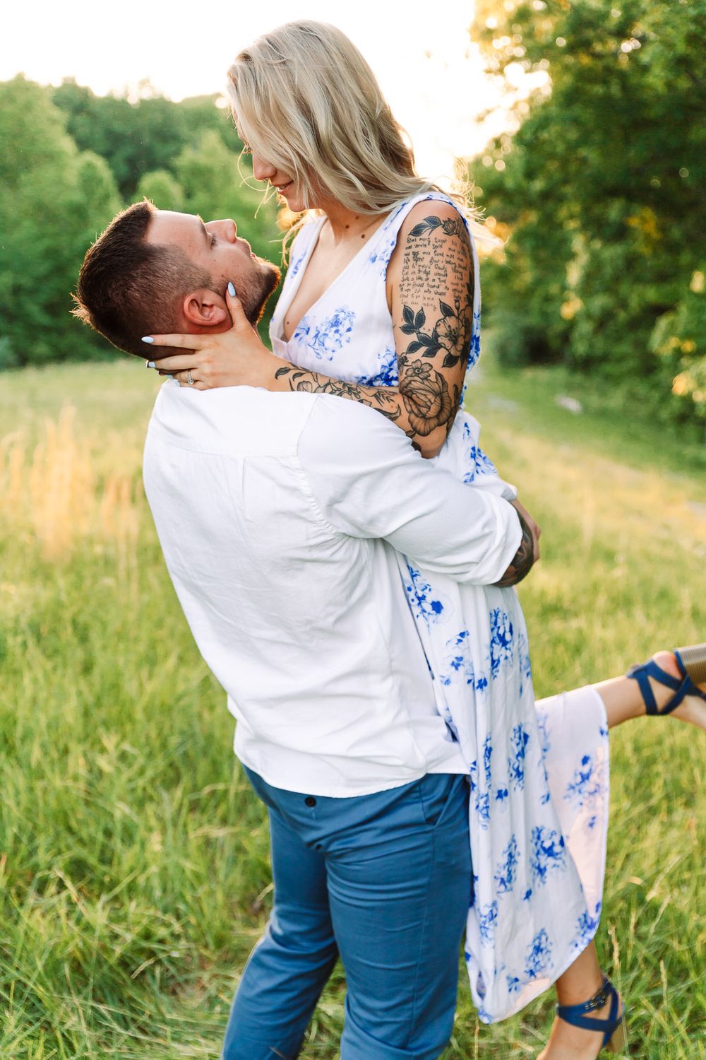 Playful couple dancing and twirling in a grassy field at sunset.
