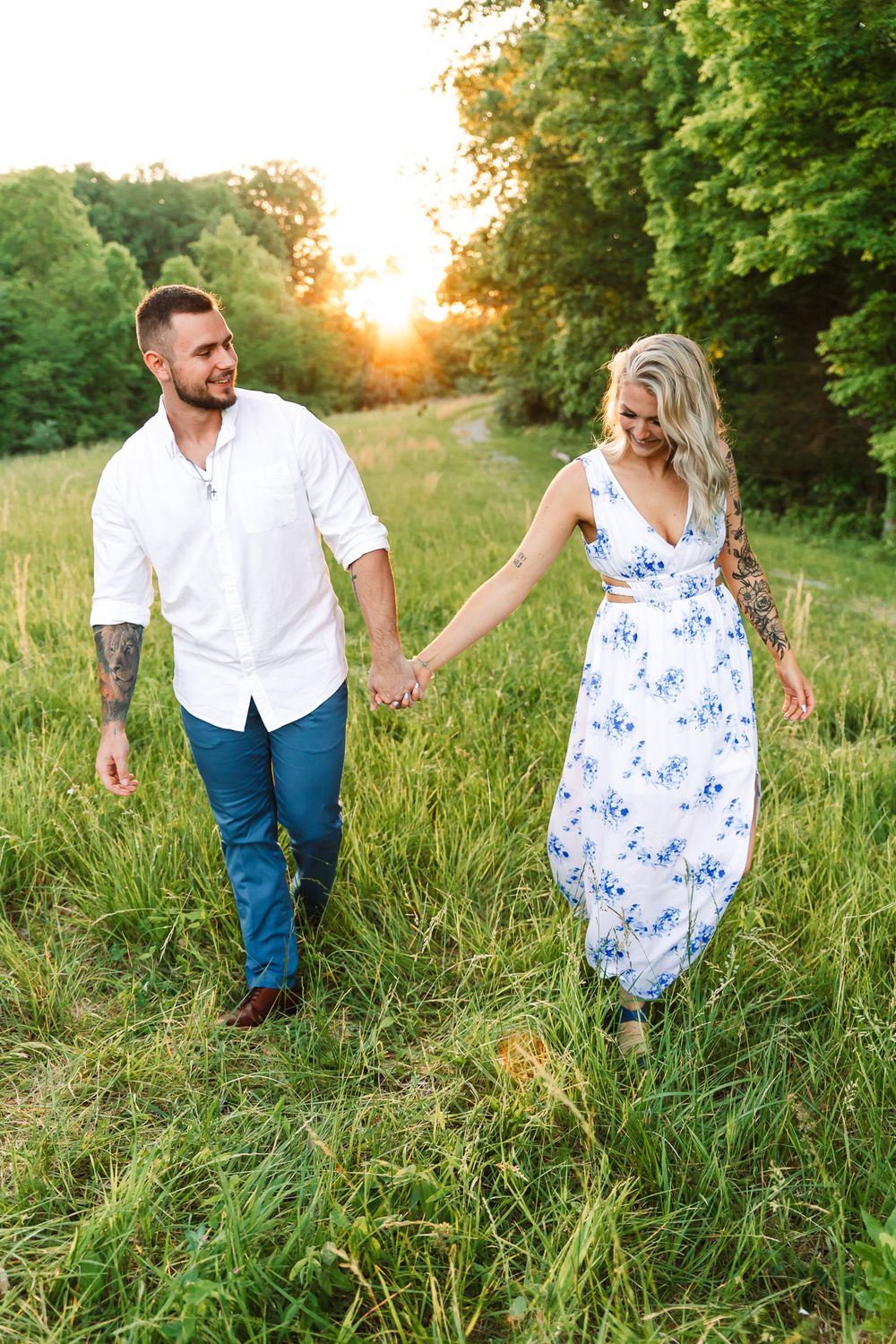 Couple walking hand in hand through tall grass during golden hour.