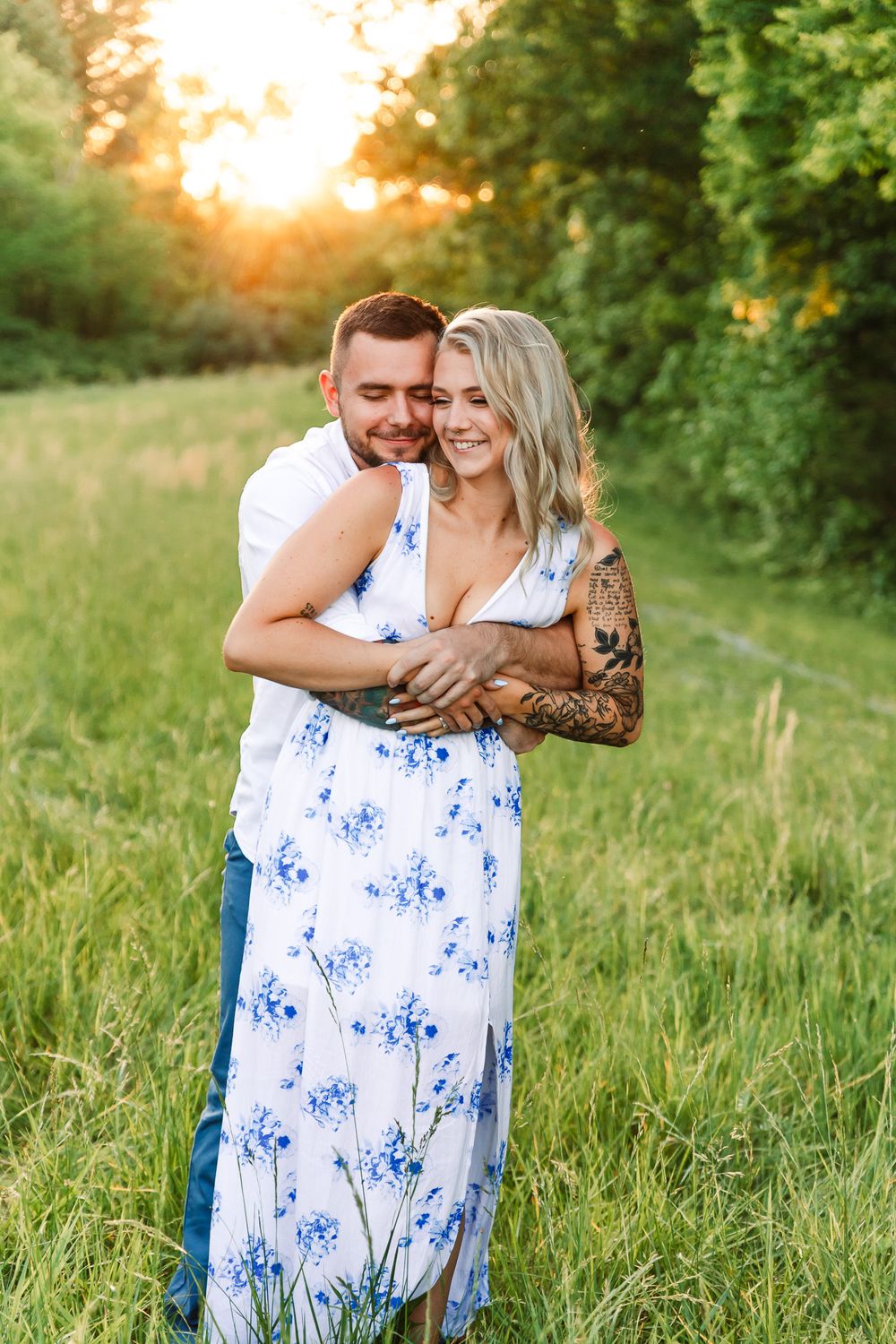 Couple sharing tender moments in a sunlit field wearing coordinated white and blue outfits.