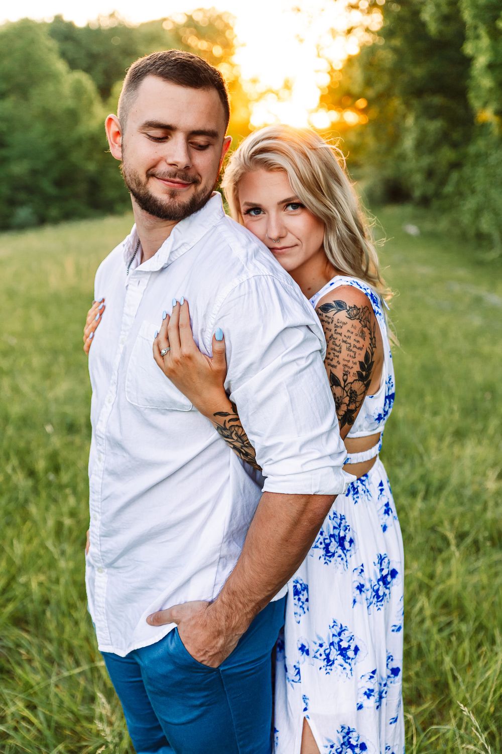 Couple embracing in a grassy field during sunset wearing white and blue.