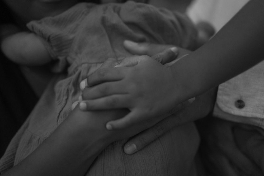 A close-up black and white image of hands gently resting on fabric.