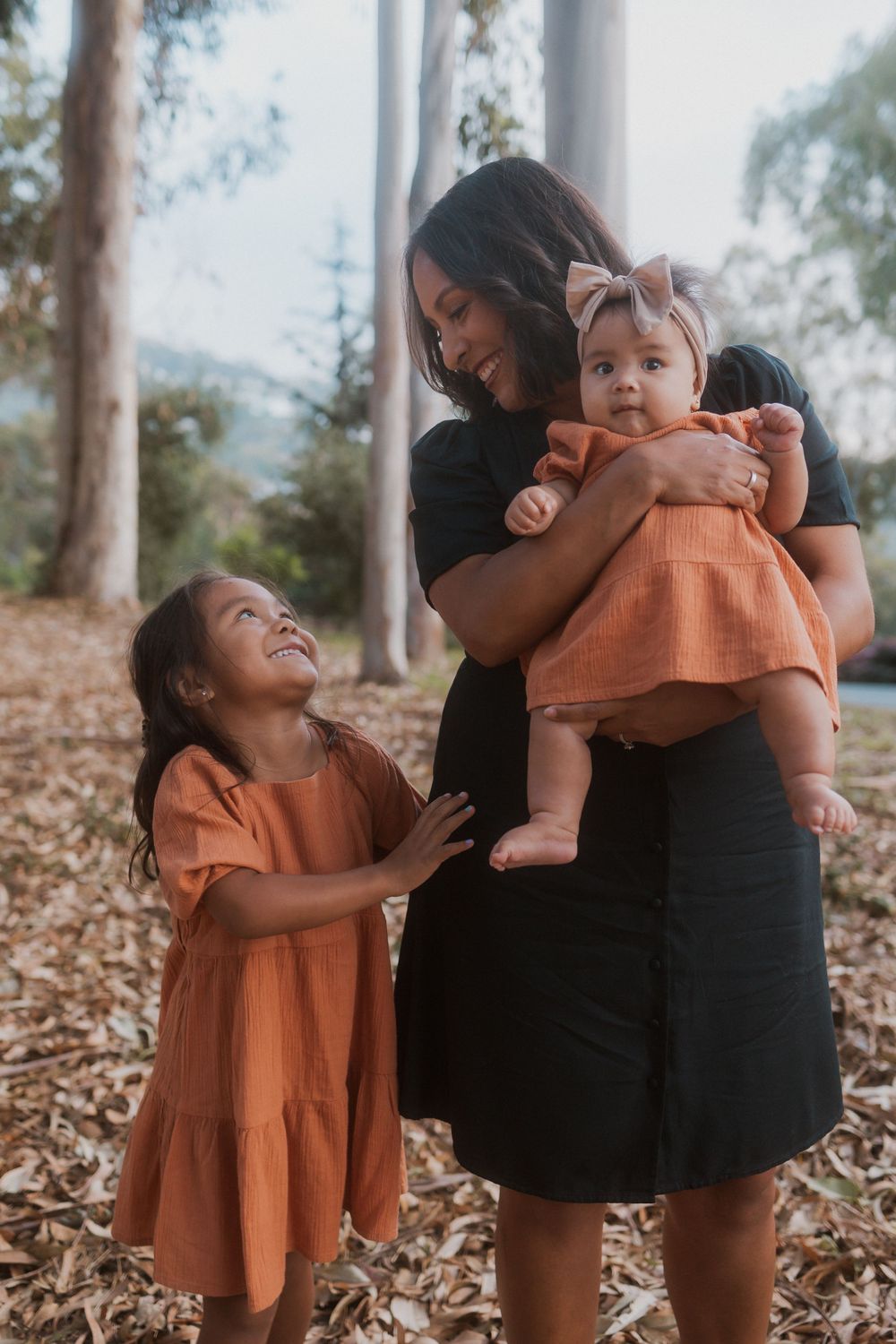 A tender family moment captured in a wooded setting with matching coral-colored dresses.